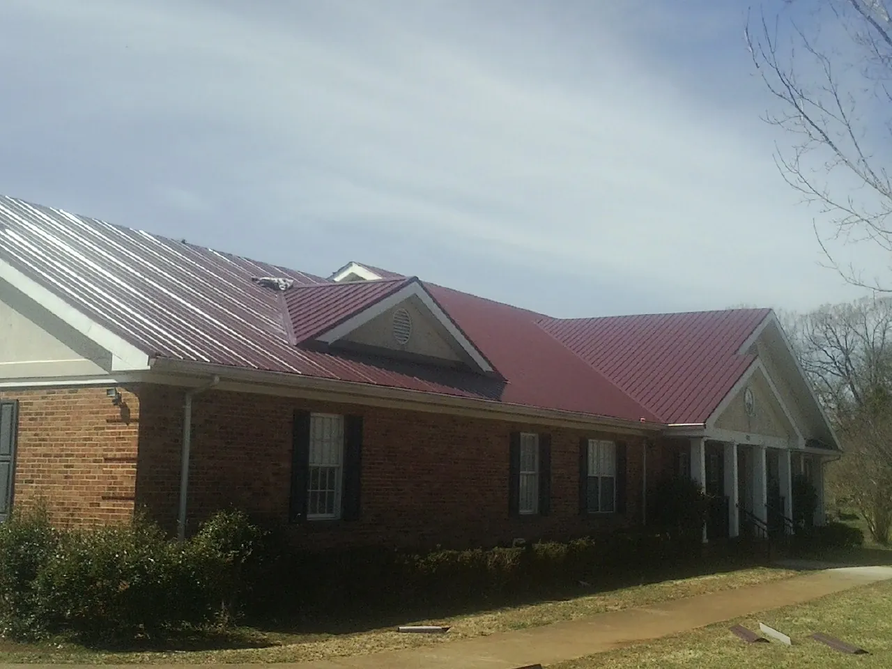 Red metal roof with gabled entries on a long brick building, from a Hail Damage Roof Repair job in Wishram