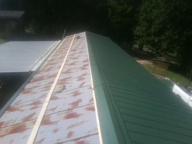 Old rusted panels beside newly installed green metal roofing — Wind Damage Roof Repair by Roofing Brothers in Wishram