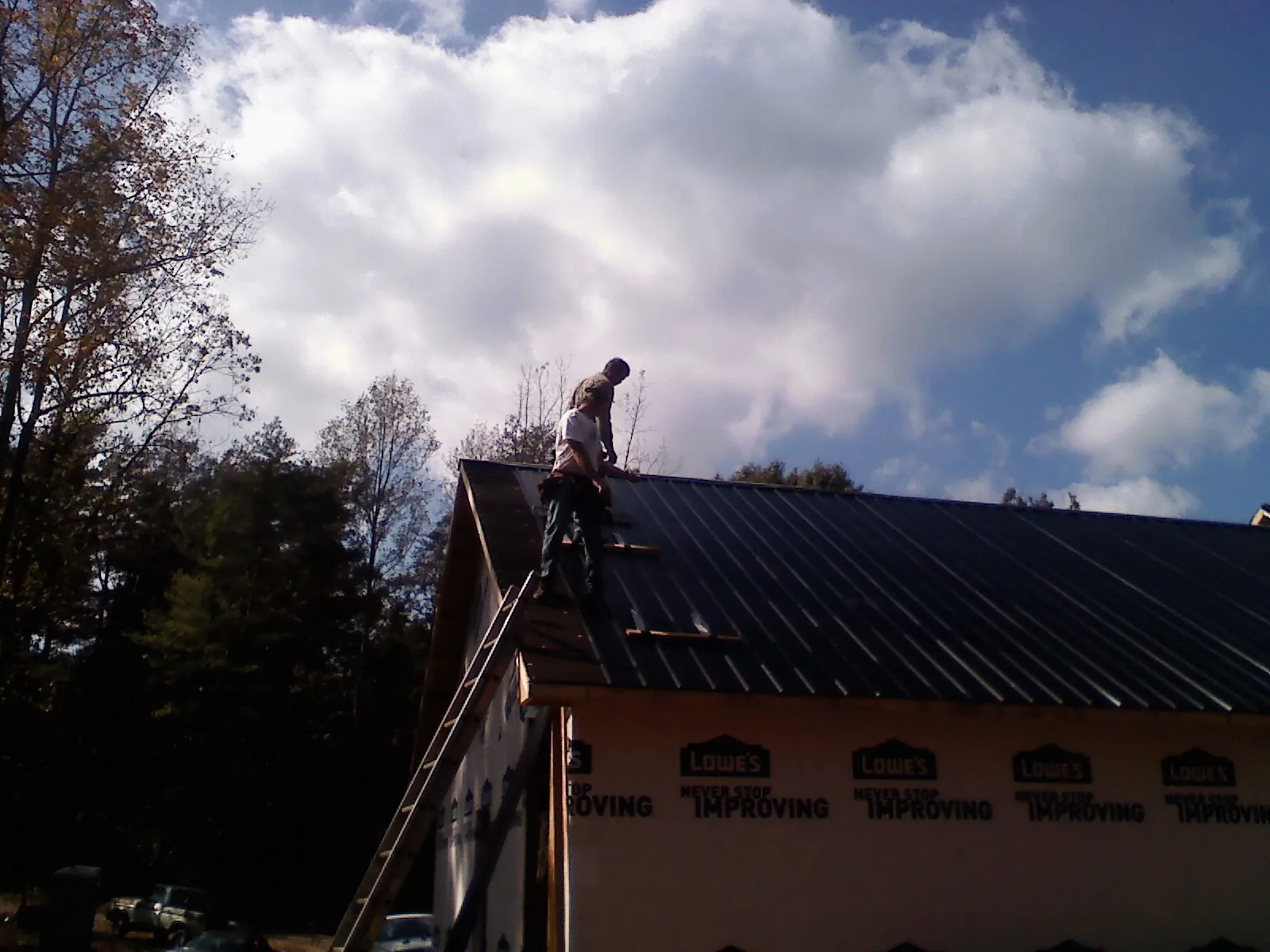 Roofer fastening dark metal panels high against a cloudy sky, from a Roof Inspection job in Wishram