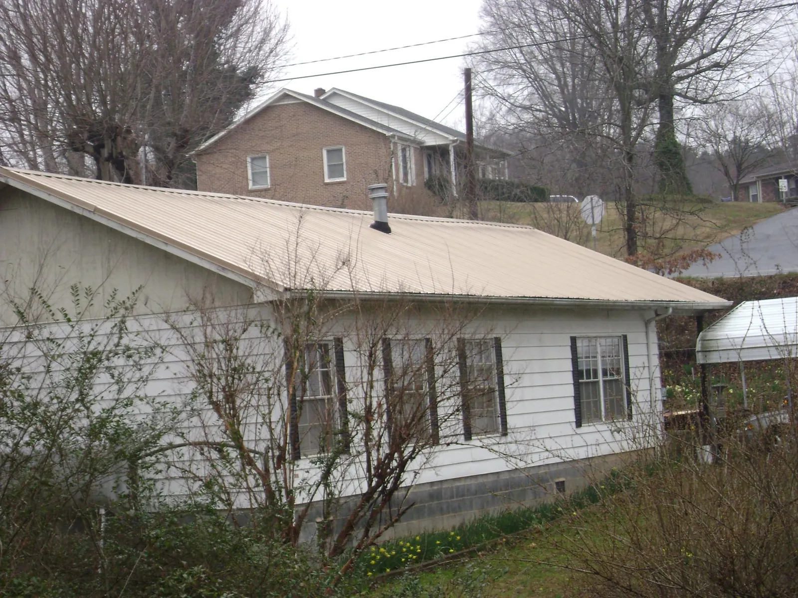 Tan metal roof on a white sided house set into a hillside — Commercial Roofing by Roofing Brothers in Wishram